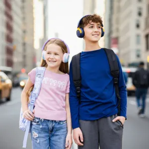 Divi bērni ar myFirst CareBuds Max virs auss liekamām austiņām un mugursomām, ejot pa pilsētas ielu.
