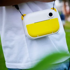 appareil photo pour enfants myFirst Camera Insta Wi jaune avec objectif circulaire et dragonne, porté sur une chemise blanche