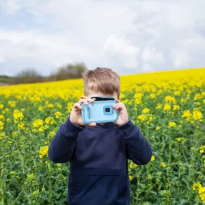 myFirst Camera 50 i ljusblått, hållen av ett barn utomhus på ett fält med gula blommor