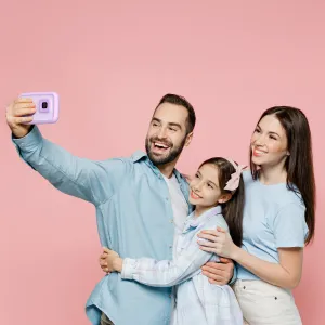myFirst Camera 50 lila selfiekamera för barn som hålls upp för en familjeselfie mot en rosa bakgrund