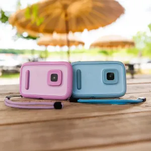 myFirst Camera 50 barnkamera i rosa och blått med handledsremmar, visad på ett träbord utomhus